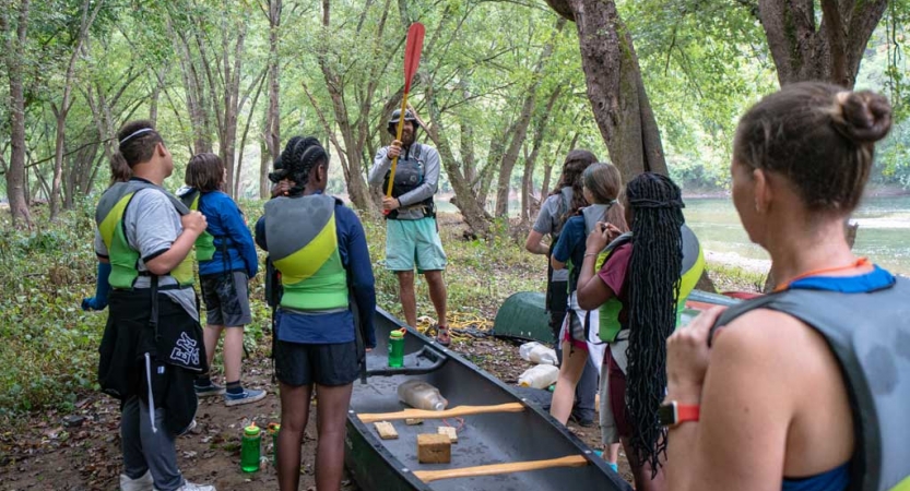 a group of teens listens to an instructor on a canoeing adventure for teens